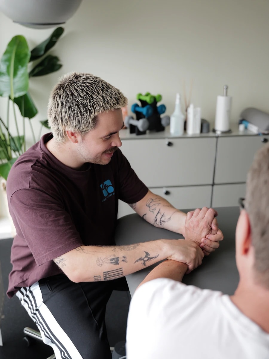 Therapeut behandelt den Arm eines Patienten und ist dabei im Gespräch.