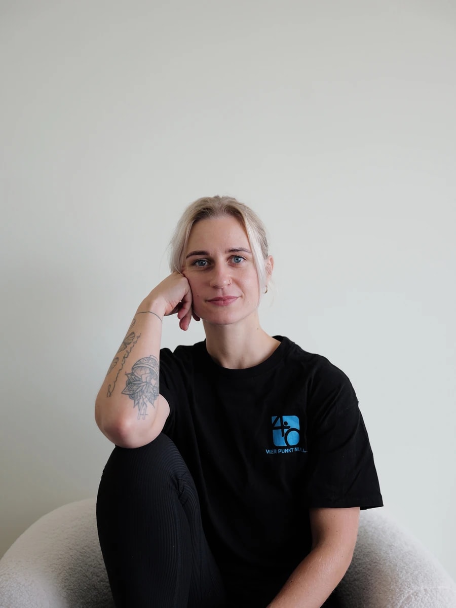 Therapeutin von Vier Punkt Null im Praxis-Shirt, sitzend, blickt in die Kamera.