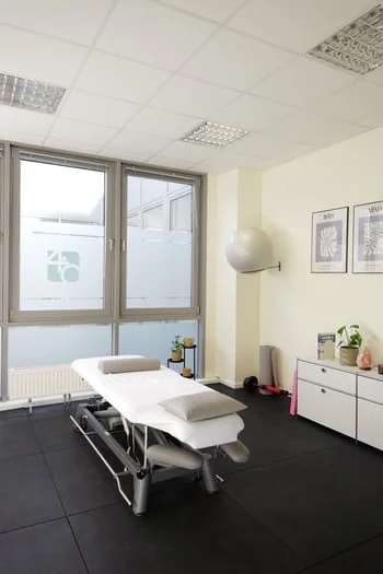 Behandlungs­raum mit Therapie­liege, Pezzi­ball und Fenster mit Vier-Punkt-Null-Logo.