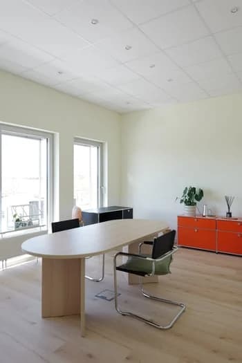 Beratungsraum mit Holztisch, Stühlen und orangenem USM-Sideboard.