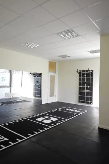 Großer Trainingsraum mit schwarzem Sportboden, Sprossengitter und Hyrox-Markierung.